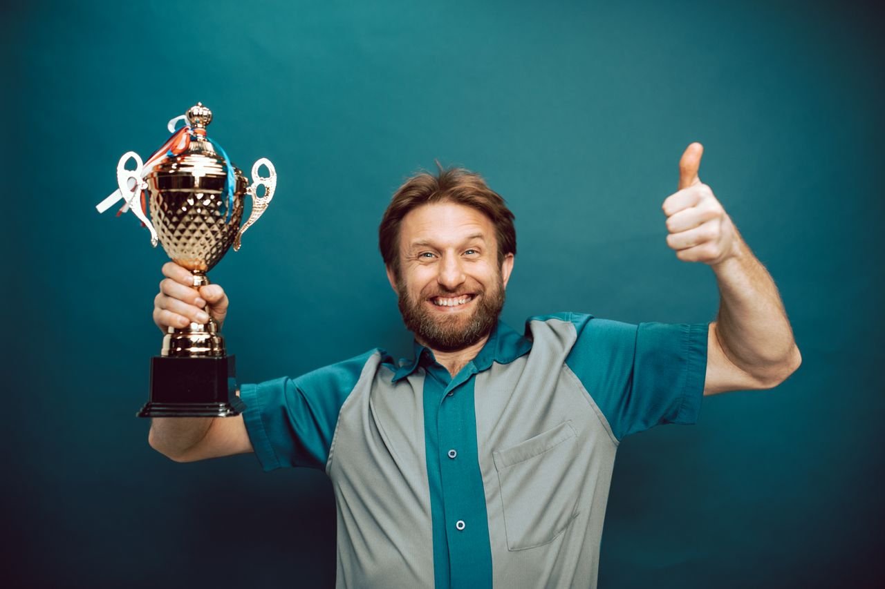 Mastering the First Impression: Your intriguing post title goes here Smiling man holding a trophy and giving a thumbs up gesture against a blue backdrop.